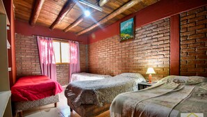Una habitación con dos camas, una pared de ladrillo, techo de madera y un cuadro.