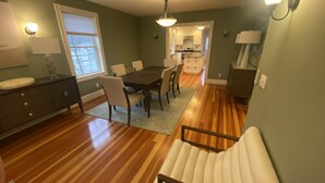 Un comedor con una mesa y sillas de madera, una cocina al fondo y un pasillo que lleva a otra habitación.