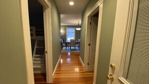 Un pasillo con suelo de madera, un comedor con mesa y sillas, y una escalera que sube a otro nivel.