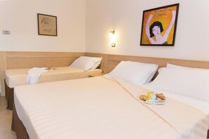 Hotellihuone, jossa on kaksi erillistä sänkyä, sängynpääty, seinään kiinnitetty valaisin ja kehystetty taideteos.