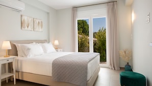 Un dormitorio con cama, mesitas de noche, una ventana con cortinas y vista a la vegetación.