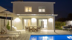 Una casa de dos pisos con piscina, mobiliario exterior y un patio cubierto.