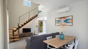 Una sala de estar moderna con una mesa de comedor de madera, sillas blancas, un sofá gris, una escalera y un televisor de pantalla plana.