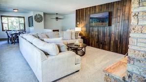A living room with a sectional sofa, a round coffee table, a fireplace, and a dining area with a table and chairs.