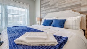 Un lit bien fait, recouvert d’une couvre-lit bleue et blanche, d’un plaid blanc et agrémenté de deux coussins bleus.
