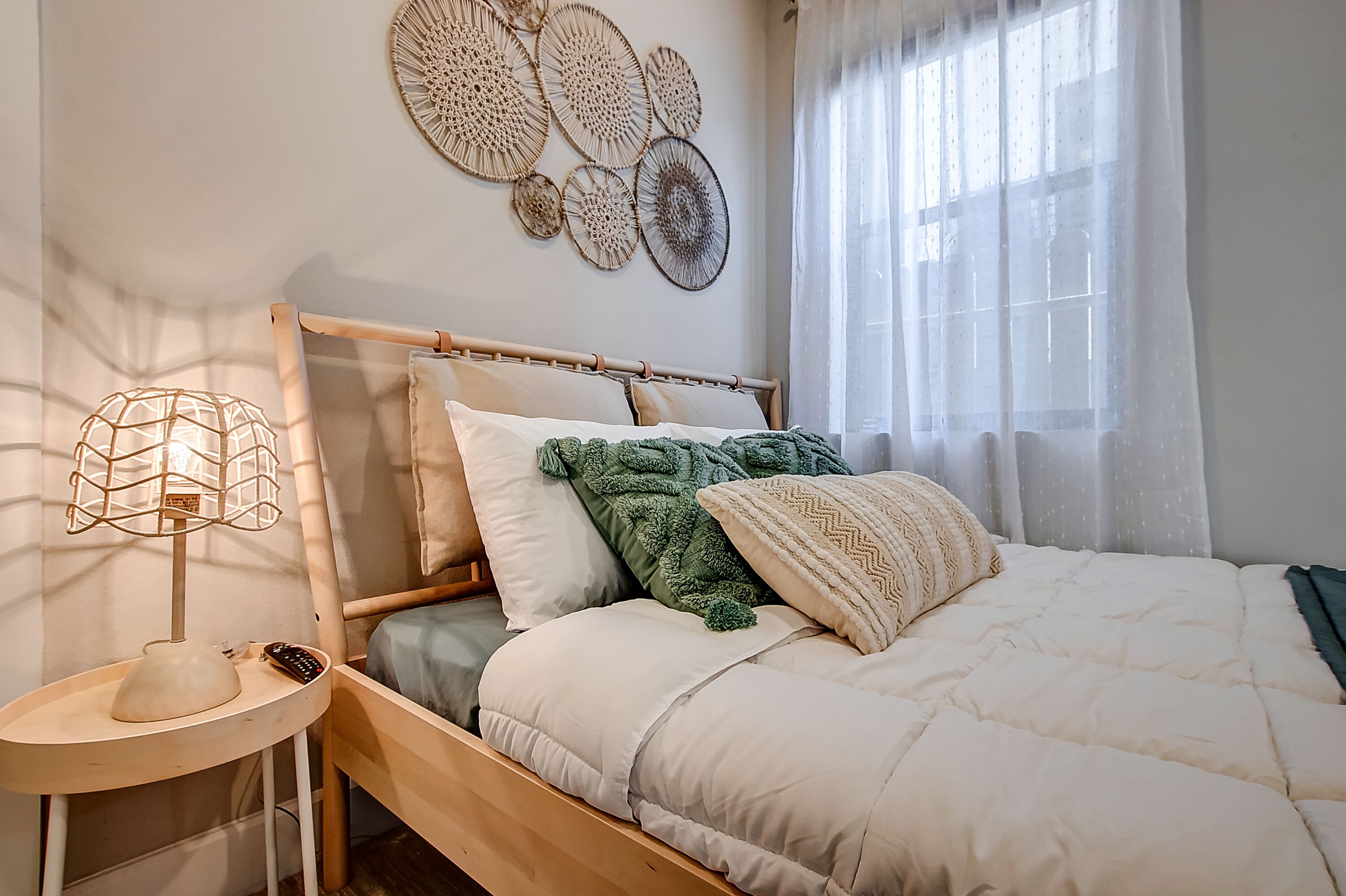 Una cama bien hecha con un cabecero de madera, una lámpara de noche y una obra de arte en la pared superior.