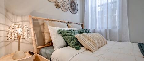 Una cama bien hecha con un cabecero de madera, una lámpara de noche y una obra de arte en la pared superior.