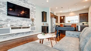 Un salon moderne avec un téléviseur à écran plat fixé à un mur texturé, un canapé, une table basse et un coin cuisine en arrière-plan.