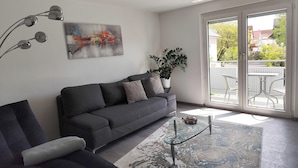 Una sala de estar moderna con un sofá gris, una mesa de centro de vidrio, un cuadro abstracto grande y una planta en maceta.
