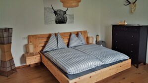 Camera da letto con un letto di legno, una lampada in fibra naturale, un teschio di cervo appeso al muro e un quadro con un animale.
