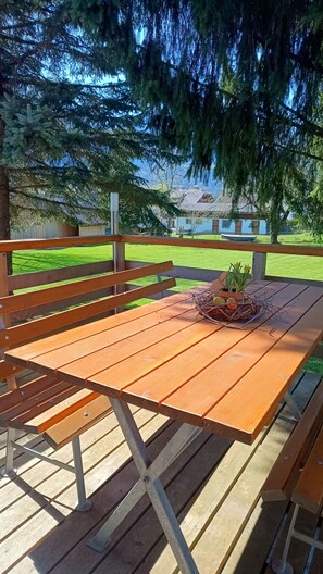 A wooden picnic table with benches, surrounded by a wooden fence and a grassy lawn.