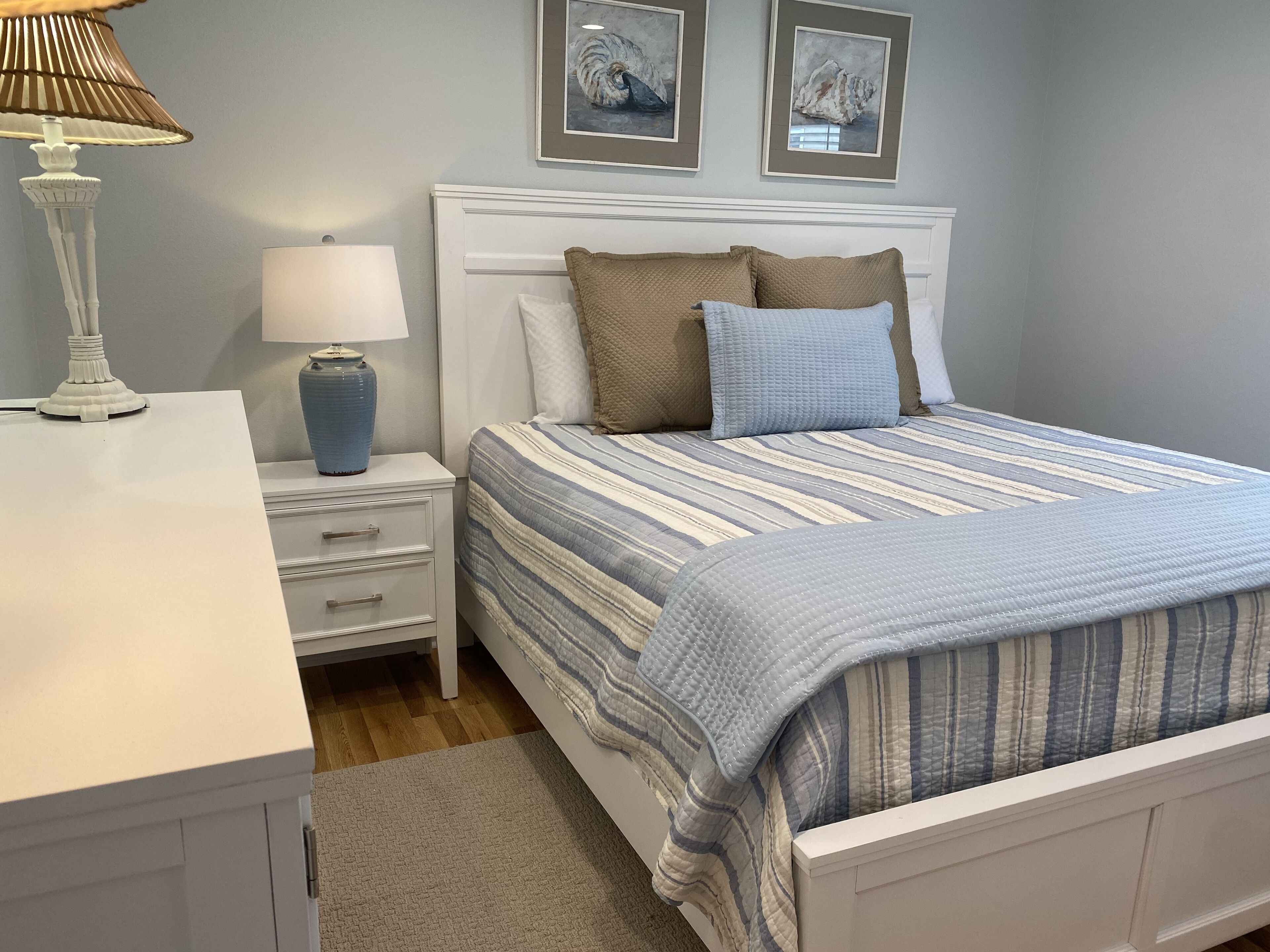A neatly arranged bedroom with a bed, bedside table, lamp, and framed artwork on the wall.