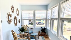 A sunlit room with wicker furniture, large windows, and decorative mirrors.