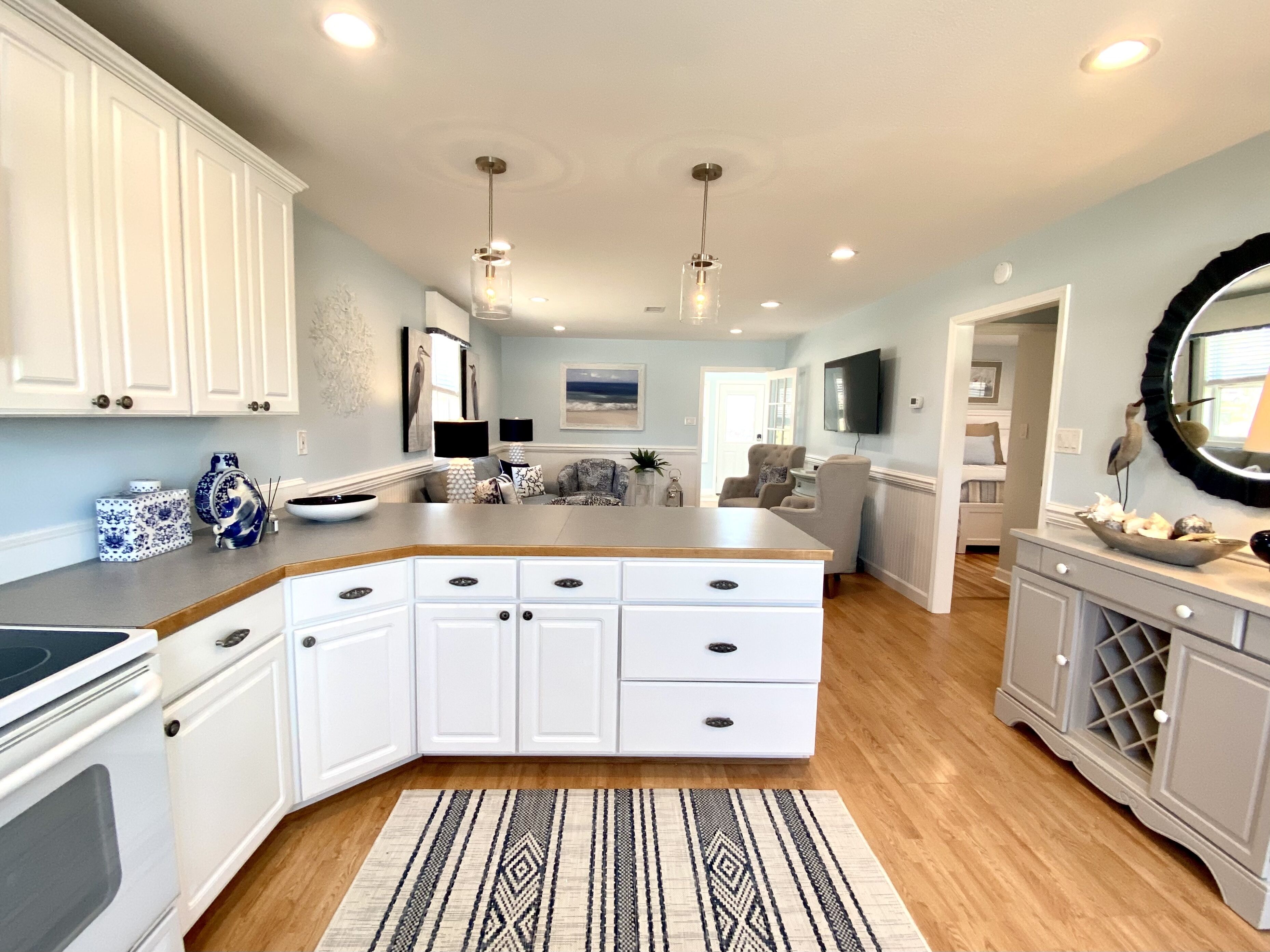 A modern kitchen with white cabinetry, a central island, pendant lighting, and a patterned rug.