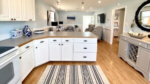 A modern kitchen with white cabinetry, a central island, pendant lighting, and a patterned rug.