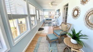 A spacious hallway with large windows, a ceiling fan, and a seating area with a sofa and chairs.
