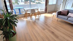 Un amplio salón con balcón, suelo de madera, un sofá, una mesa de comedor con sillas y una planta en maceta.