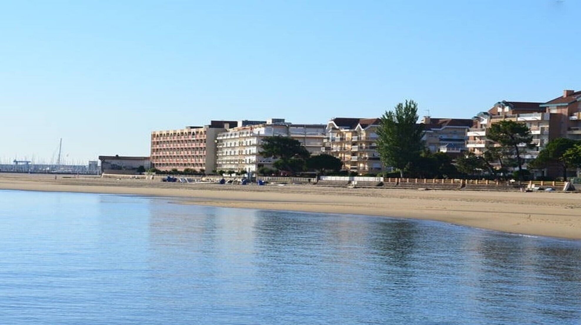 A beachfront hotel with multiple floors, a sandy beach in the foreground, and a clear sky.