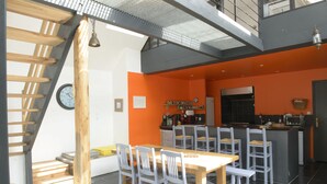 A modern kitchen with a central island, a dining area with a wooden table and chairs, and a staircase leading to an upper level.