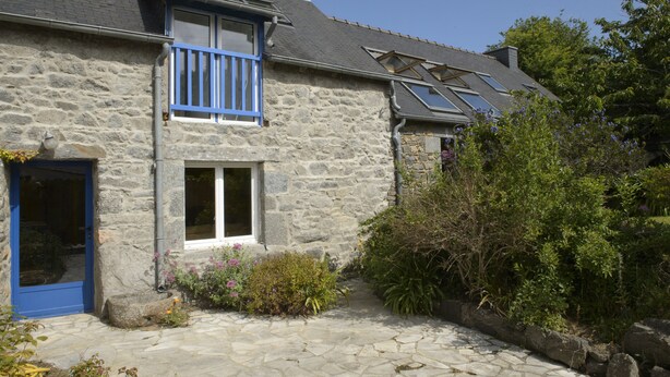 A stone house with a blue door and windows, a stone pathway, and surrounding greenery.