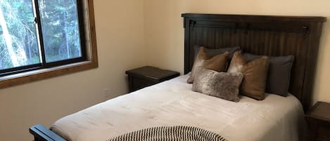 Un dormitorio con una cama grande, una ventana con vistas a árboles, un cabecero de madera y una mesita de noche.
