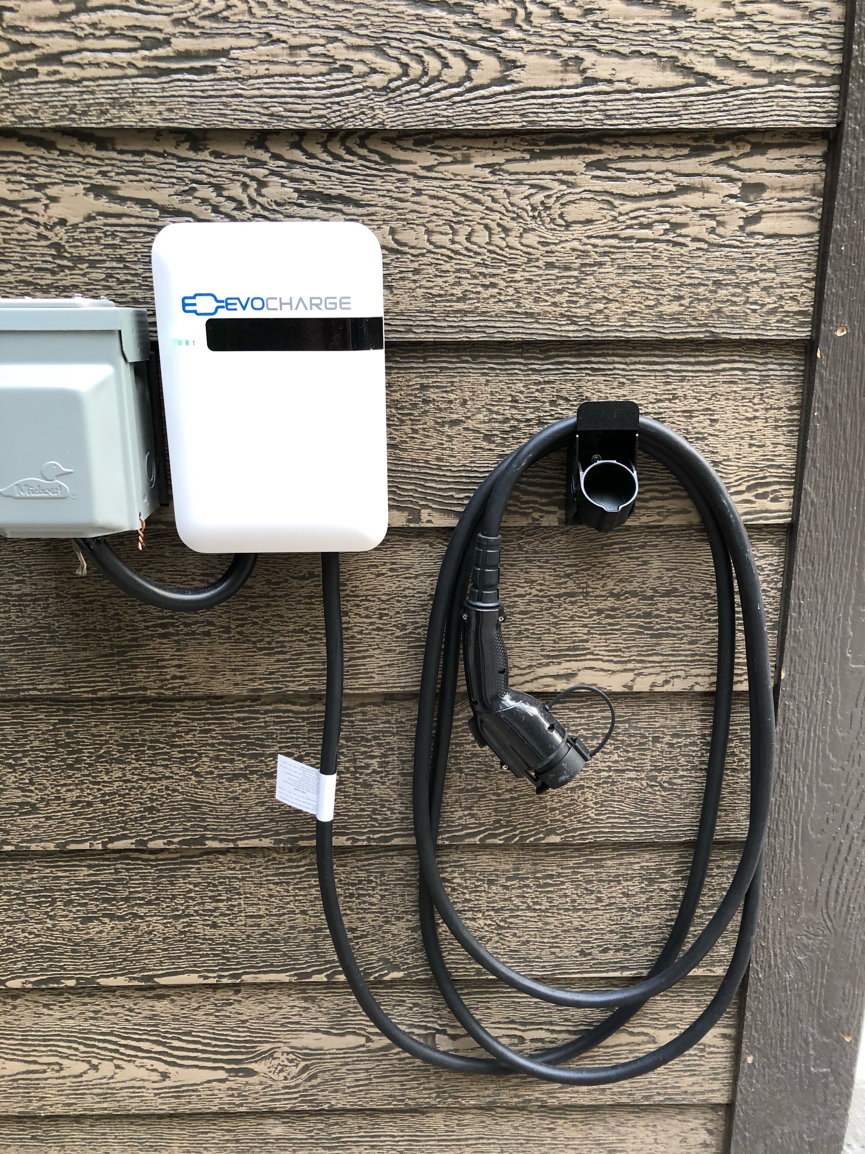 An EV charger connected to a wall-mounted box with a cable.