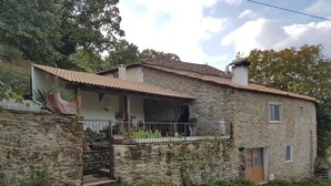 Una casa de pedra amb teulada de rajola, un balcó amb barana de metall i una petita zona de jardí.