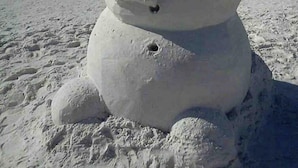 A snowman sculpture on a beach with the ocean in the background.