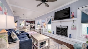 A living room with a fireplace, a television, and a dining area with a kitchen in the background.