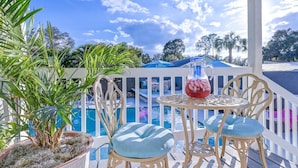 A poolside area with a table and chairs, a potted plant, and a view of a swimming pool.