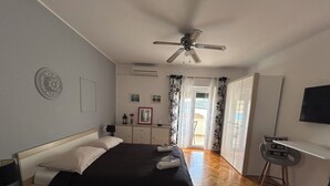 Un dormitorio con cama, escritorio, silla, ventilador de techo y vistas al exterior.