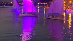 Tres veleros con velas iluminadas en una superficie acuática tranquila al anochecer.