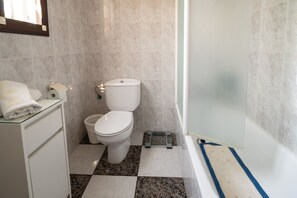 A bathroom with a toilet, a glass cabinet, a shower area, and a tiled floor.