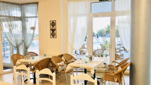 Ein Restaurant mit Korbstühlen und Tischen, großen Fenstern mit durchsichtigen Vorhängen und einem Ausgangsschild.
