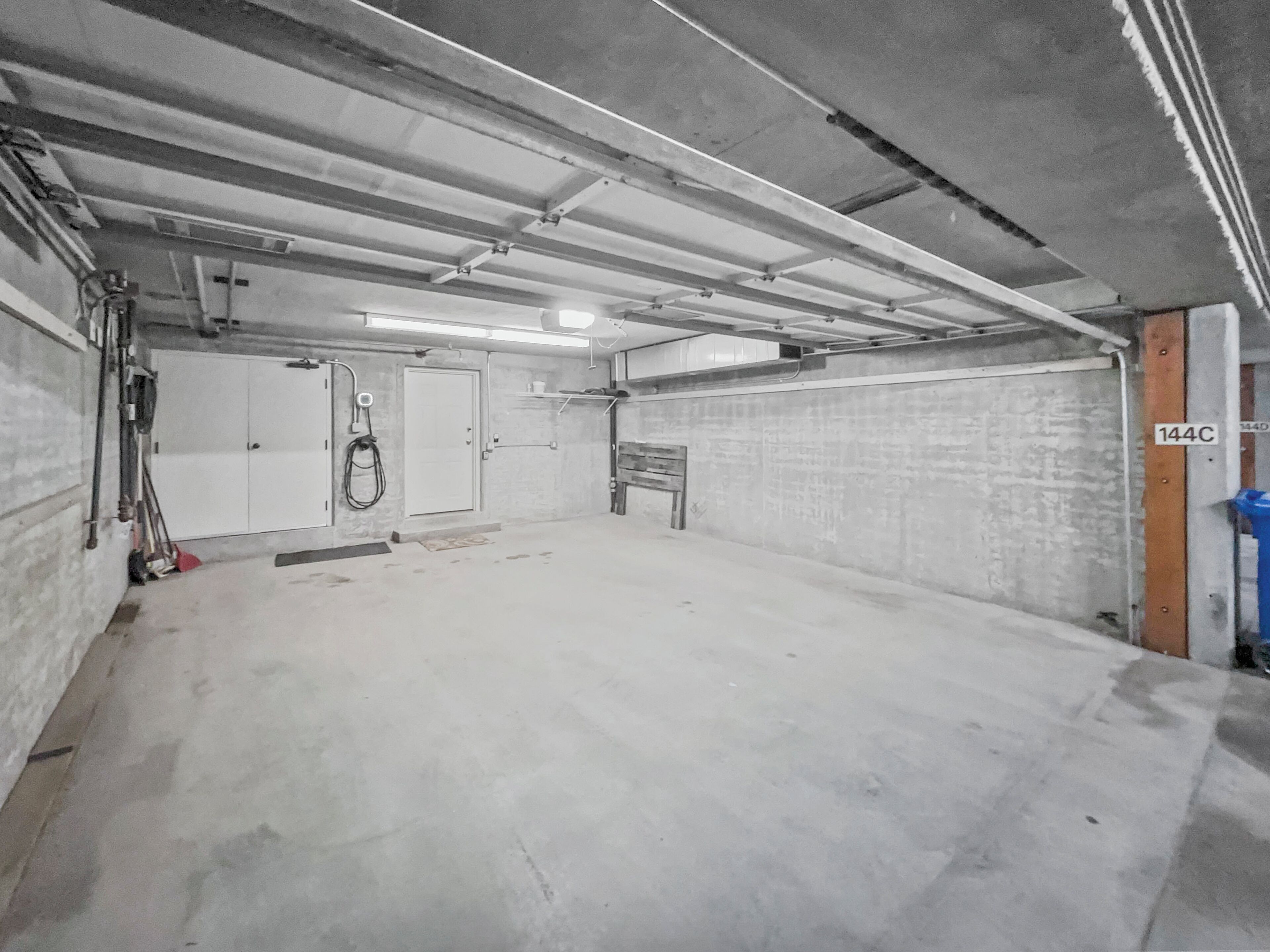 A spacious, empty parking garage with concrete floors and walls, a door labeled "144C", and overhead lighting.