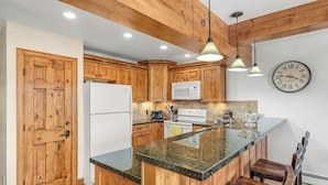 A kitchen with wooden cabinets, a white refrigerator, a microwave, a stove, and a clock on the wall. - Charming 2BR/2BA Snowmass Condo with Shared Hot Tub (Snowmass Village)