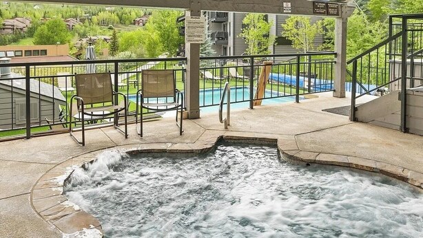 A hot tub area with a view of a swimming pool and a covered deck with chairs. - Charming 2BR/2BA Snowmass Condo with Shared Hot Tub (Snowmass Village)