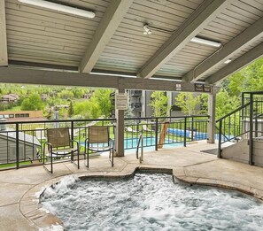 Un espace avec un bain à remous offrant une vue sur une piscine et une terrasse couverte avec des chaises.