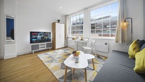 A modern living room with a TV, dining area, and large windows. - Studio Apartment Blue (London)