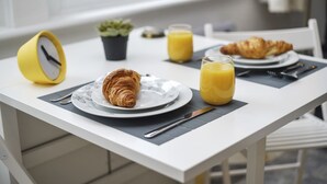A breakfast setting with croissants, orange juice, and a yellow clock on a white table. - Studio Apartment Blue (London)