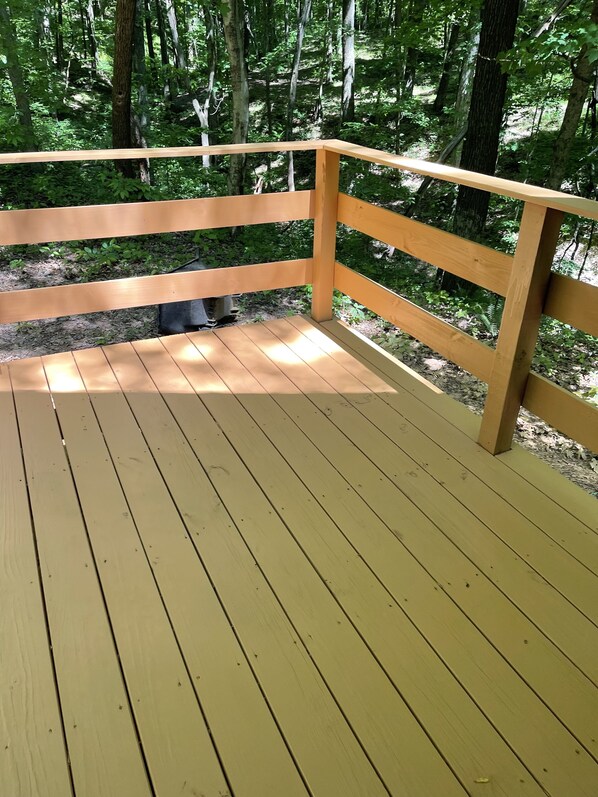 A wooden deck with railings, surrounded by dense greenery.