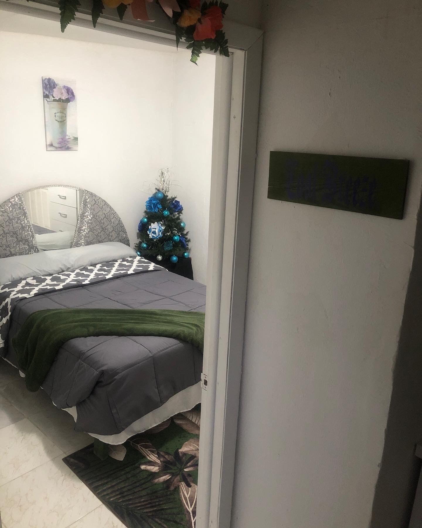 Un dormitorio con una cama, un pequeño árbol de Navidad y un letrero en la pared.