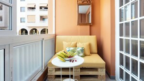 Ein Balkon mit einem weißen Tisch, einem gelben Sofa und einer Obstschale.