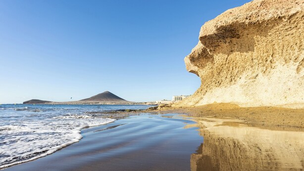 Ein Strand mit einer großen Felsformation und einem Berg im Hintergrund.