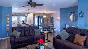 A modern living room with leather sofas, a coffee table with a vase of red flowers, and a dining area with a chandelier. - Oasis Home with Pool and Hot Tub (Lake Havasu City)
