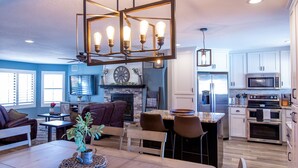 A modern kitchen with stainless steel appliances, a dining area with a wooden table and chairs, and a living room with a fireplace and blue walls. - Oasis Home with Pool and Hot Tub (Lake Havasu City)