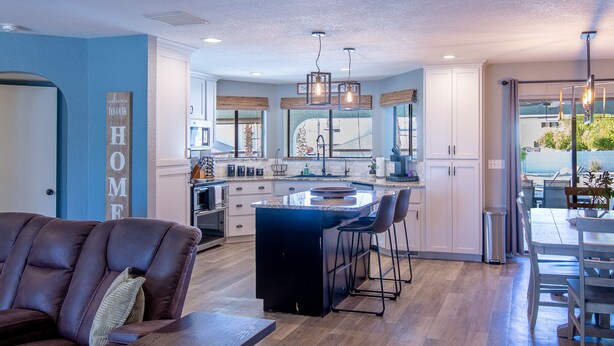 A modern kitchen with a central island, bar stools, and a dining area with a table and chairs. - Oasis Home with Pool and Hot Tub (Lake Havasu City)