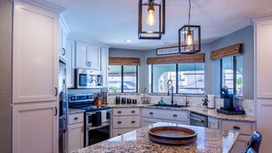 A modern kitchen with white cabinetry, granite countertops, a built-in oven, and a large island with a wooden bowl. - Oasis Home with Pool and Hot Tub (Lake Havasu City)