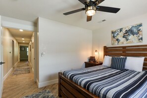 Un dormitorio con cama, mesita de noche, lámpara, ventilador de techo y un cuadro en la pared.