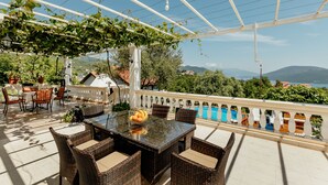 Un patio al aire libre con muebles de mimbre, una mesa de vidrio y vistas a una piscina y montañas.